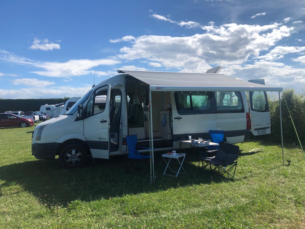 The Kiwi Blog Bus Campervan parked up on a campsite with awning and furniture out